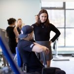 Ava Neely in the gym coaching a student on a piece of equipment