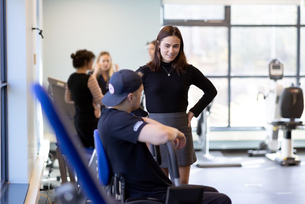 Ava Neely in the gym coaching a student on a piece of equipment