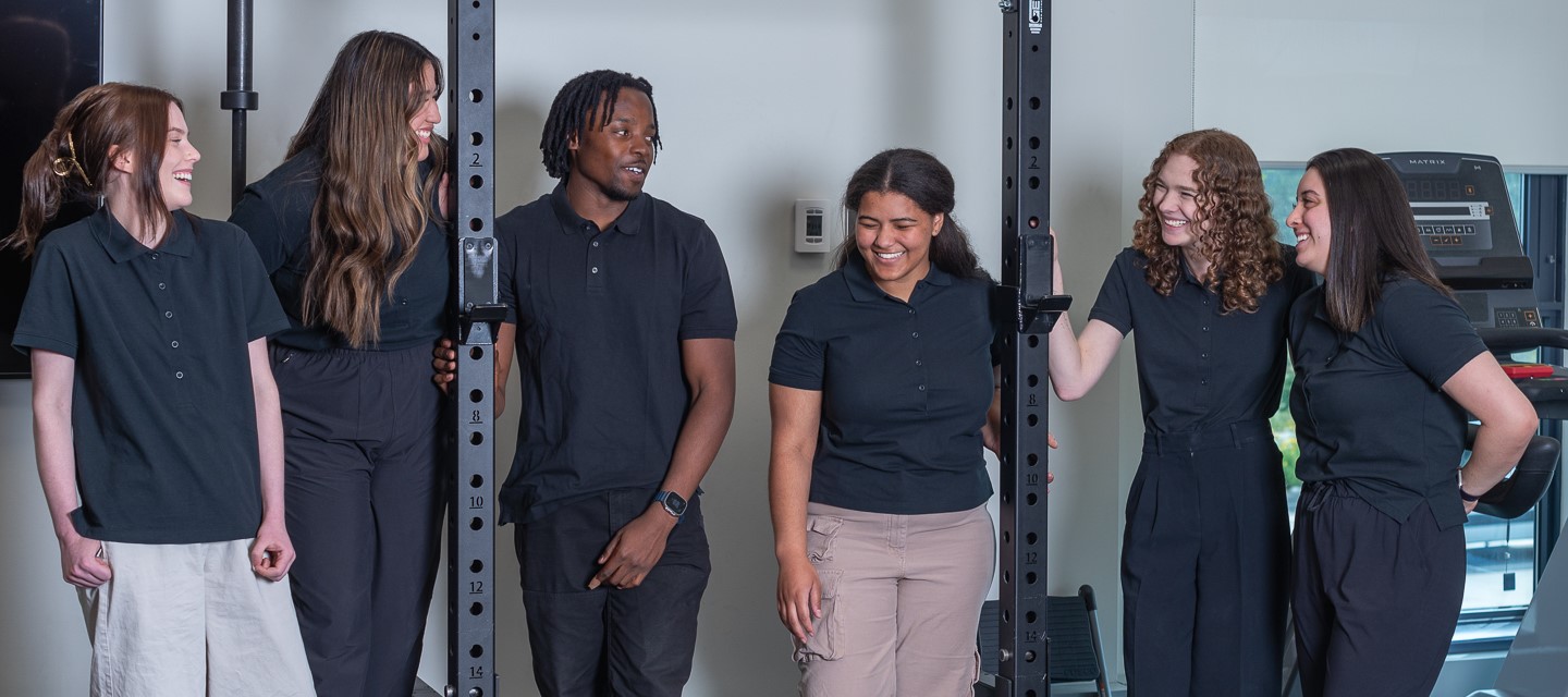 Five students standing around a squat rack in a gym.