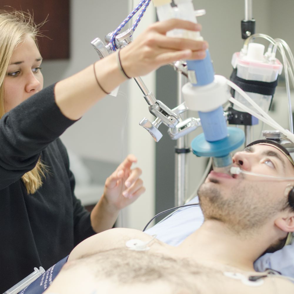 Student holding breathing tube over a participant. The breathing tube is in the participant's mouth.