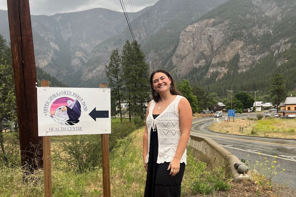 Skylar Bown standing next to Similkameen Indian Band Health Centre sign at side of the road