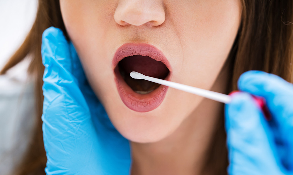 a close up of a woman having her throat swabbed for a saliva test.